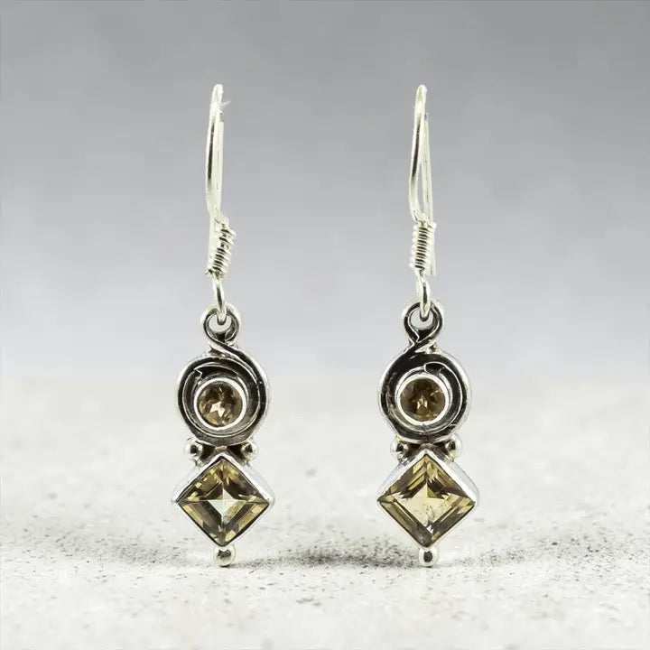 Pair of silver earrings with Citrine stones on a textured surface.