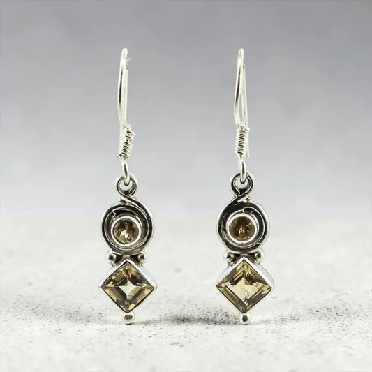 Pair of silver earrings with Citrine stones on a textured surface.