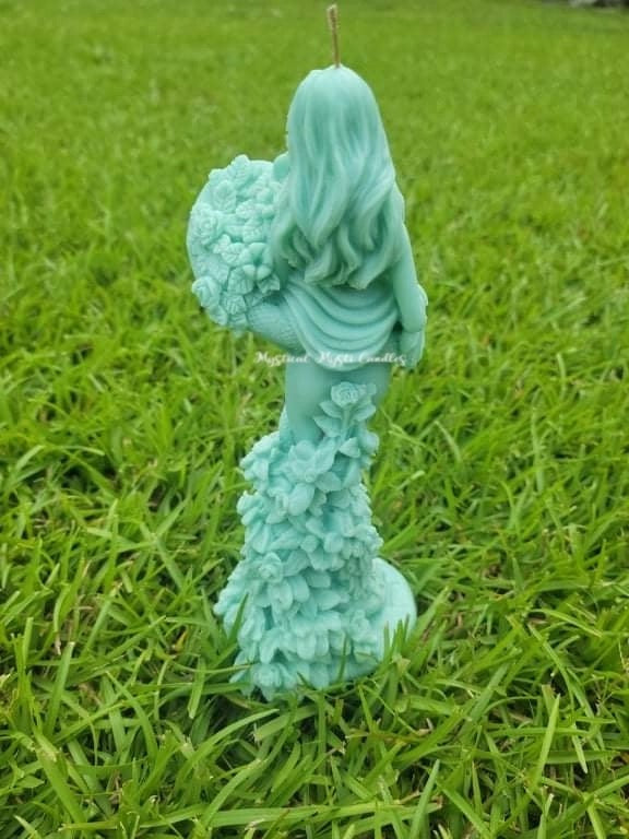 Turquoise-colored sculpture of a figure with flowers on a grassy background