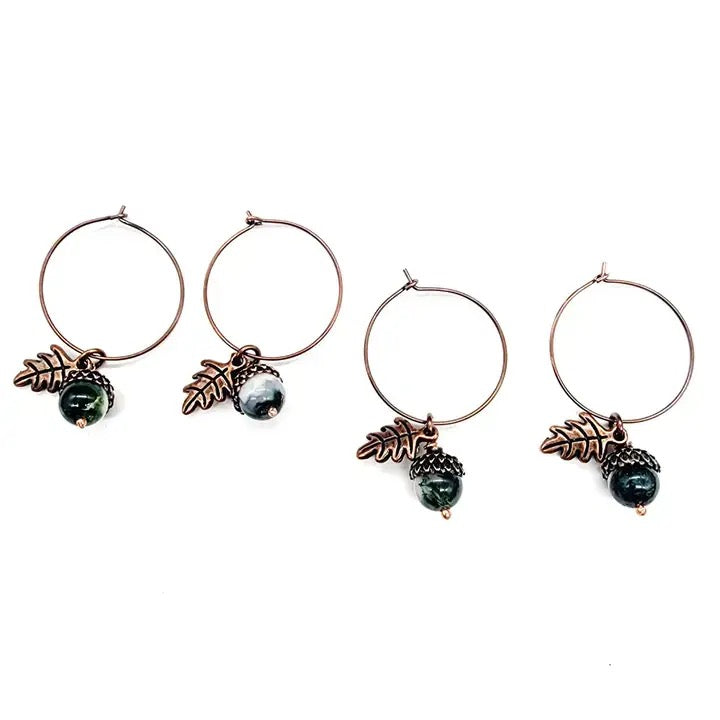 Four earrings with leaf and pine cone designs on a white background