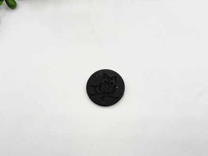 A small round black button with an embossed owl design, placed on a plain white surface.
