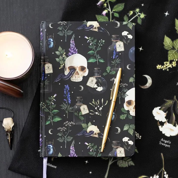 Notebook with skull and potion design on a dark surface with a candle and pen.