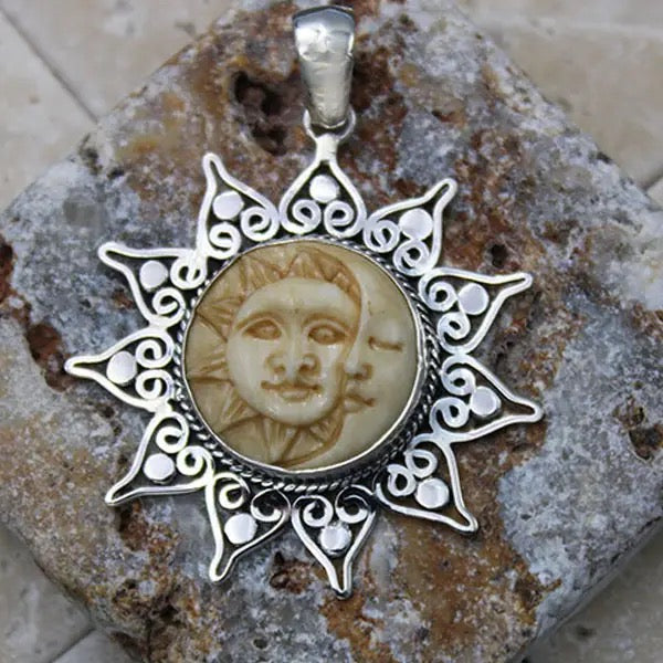 Silver pendant with face design on a stone surface