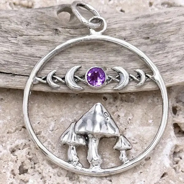 Silver pendant with mushrooms and a purple gemstone on a wooden background