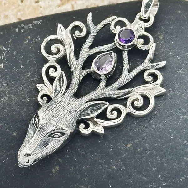 Silver deer head pendant with gemstones on a dark surface