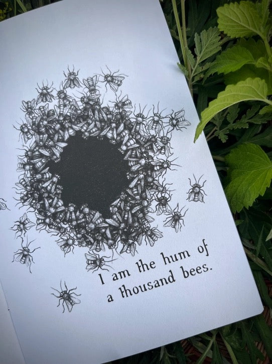 A printed card or book page with a black illustration of many bees around a dark center and the text 'I am the hum of a thousand bees,' photographed outdoors among green leaves.