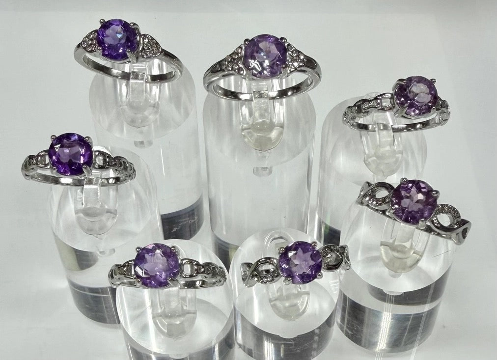 Set of silver rings with purple gemstones on clear stands against a white background