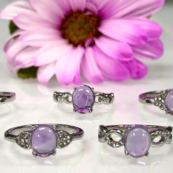 Set of silver rings with purple gemstones in front of a pink flower