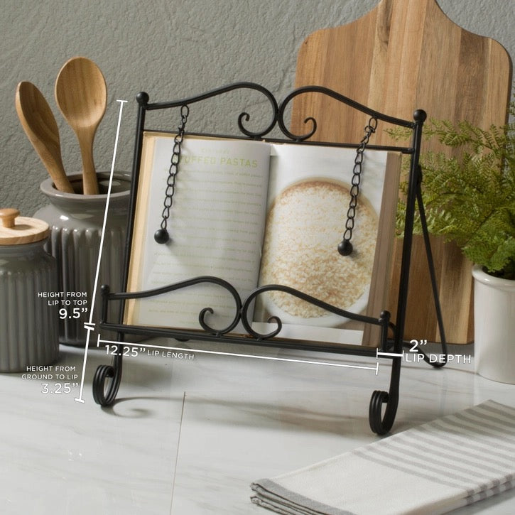 Black wrought iron book stand with hanging chain details, shown holding an open cookbook on a kitchen counter with measurement annotations overlaid.