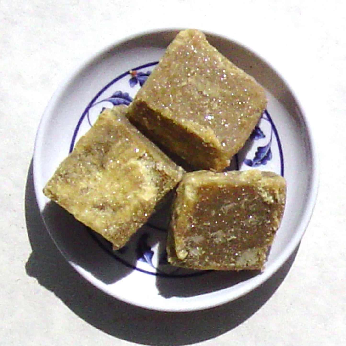 Three square pieces of a brownish incense item on a white plate with blue floral patterns.