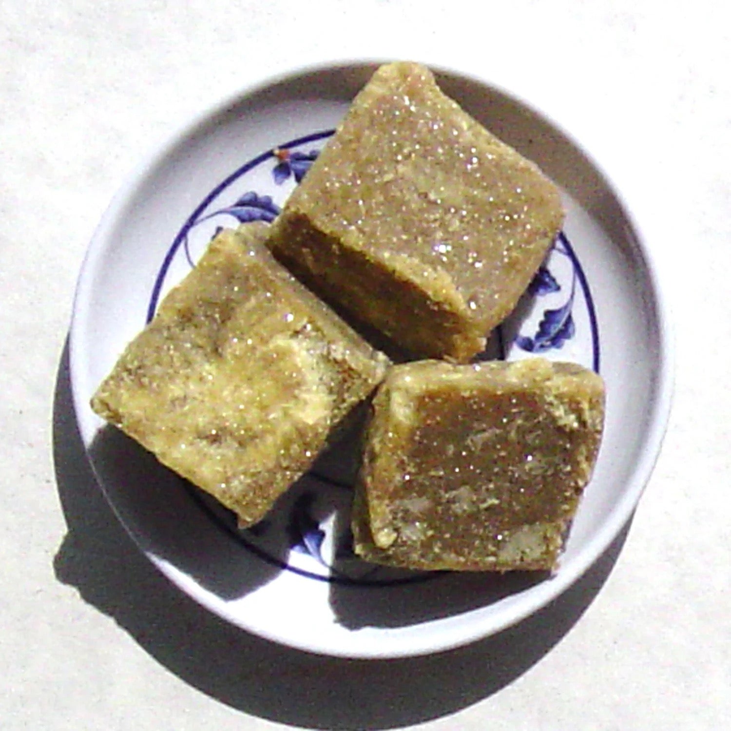 Three square pieces of a brownish incense item on a white plate with blue floral patterns.