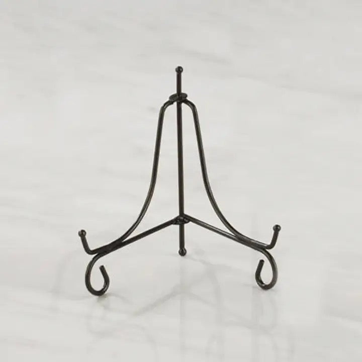 A black metal display stand with three legs and curved hooks at the ends, photographed on a light gray marble-like surface.