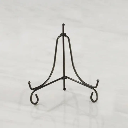 A black metal display stand with three legs and curved hooks at the ends, photographed on a light gray marble-like surface.