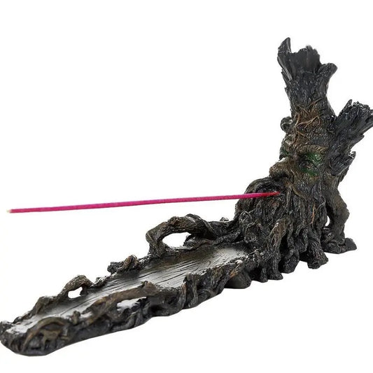 A dark, gnarled resin incense holder shaped like a weathered tree stump, with a single pink incense stick inserted into its side, set against a plain white background.