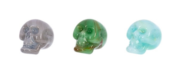 Three glass skull figurines in different colors on a white background