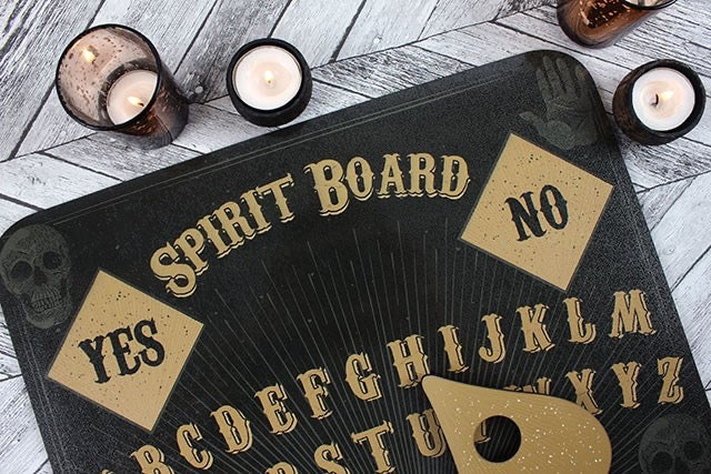 Black spirit board with gold text and letters on a wooden surface with candles.