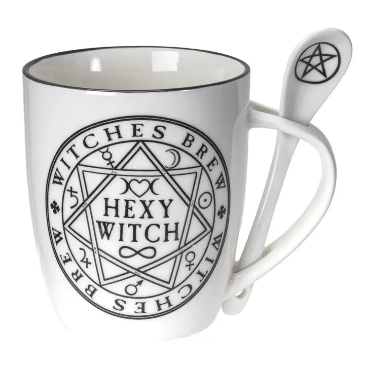 White ceramic mug with a black rim and a black printed pentagram and 'Witches Brew' design, accompanied by a matching white spoon featuring a black pentagram symbol.