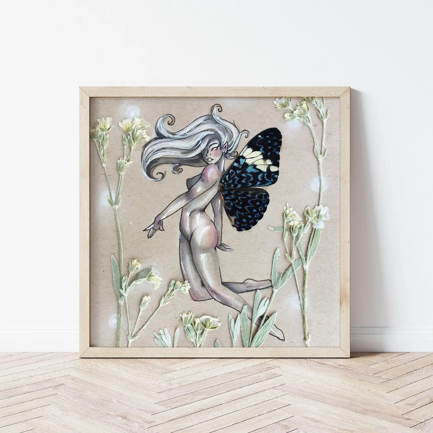 Framed artwork of a fairy with butterfly wings among flowers on a wooden floor.