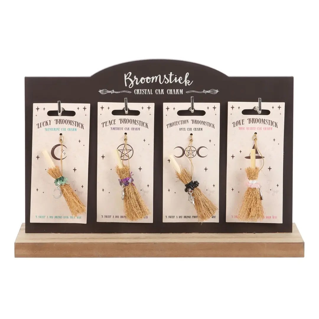 A set of four broomstick crystal car charms mounted on a dark brown display card labeled 'Broomstick Crystal Car Charm,' shown on a light wood base against a white background.
