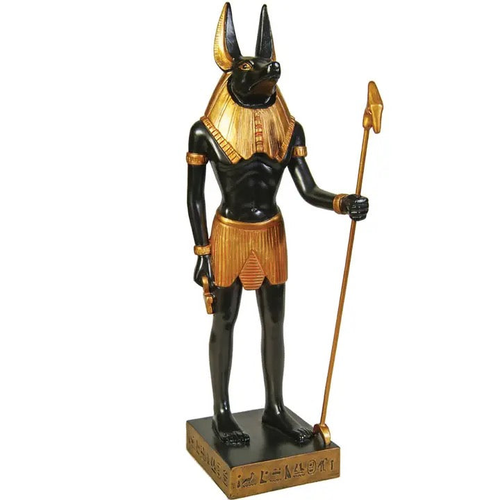 An Egyptian Anubis statue with a black body, gold collar and skirt, holding a gold staff, standing on a rectangular base with hieroglyphics.