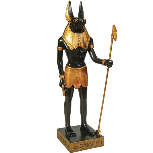 An Egyptian Anubis statue with a black body, gold collar and skirt, holding a gold staff, standing on a rectangular base with hieroglyphics.