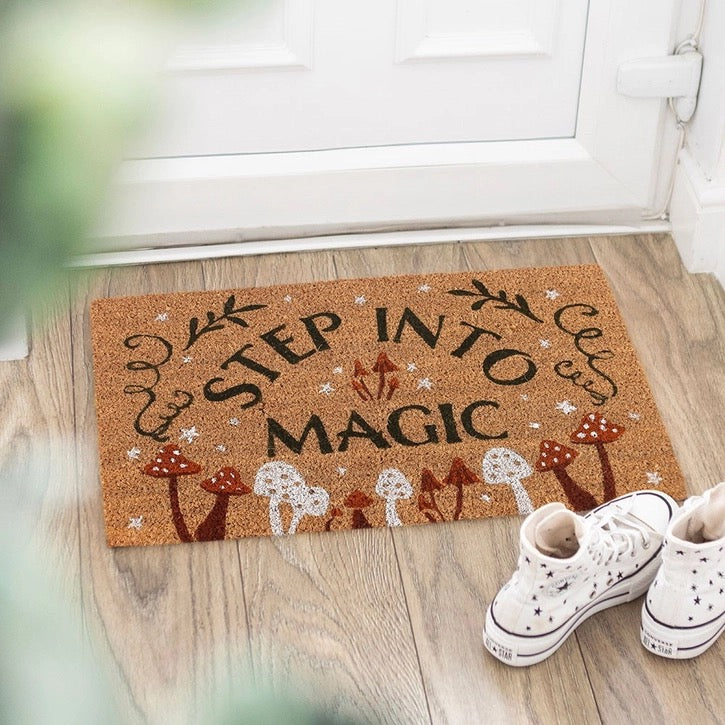Doormat with 'Step into Magic' text on a wooden floor with white shoes.
