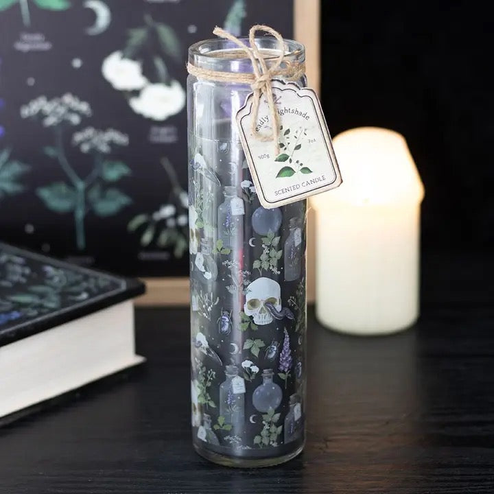 Decorative candle in a glass jar with a label on a dark surface, surrounded by books and a candle.