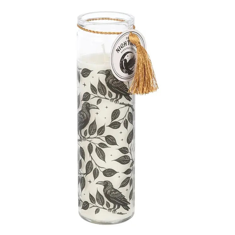 A tall glass jar candle with white wax, decorated with a black bird and leaf pattern. It has a gold tassel and a round paper tag that reads 'Night Owl Candle Co.