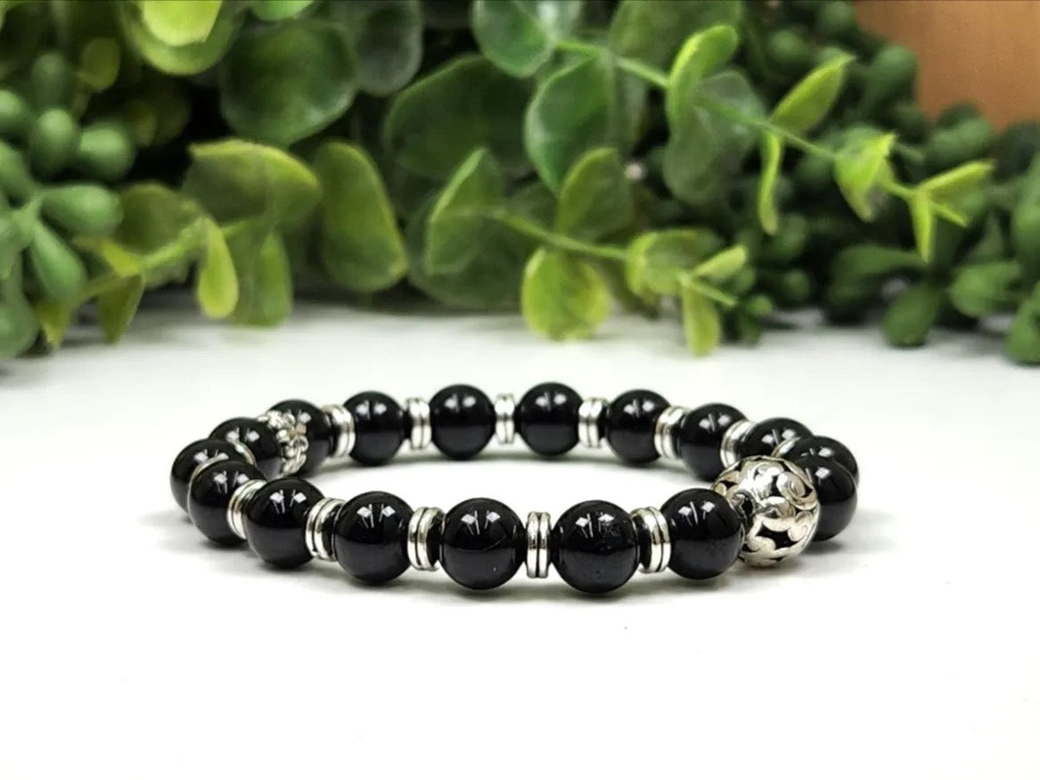 Black tourmaline bracelet with silver spacers and beads on a white table and greenery in the back ground.