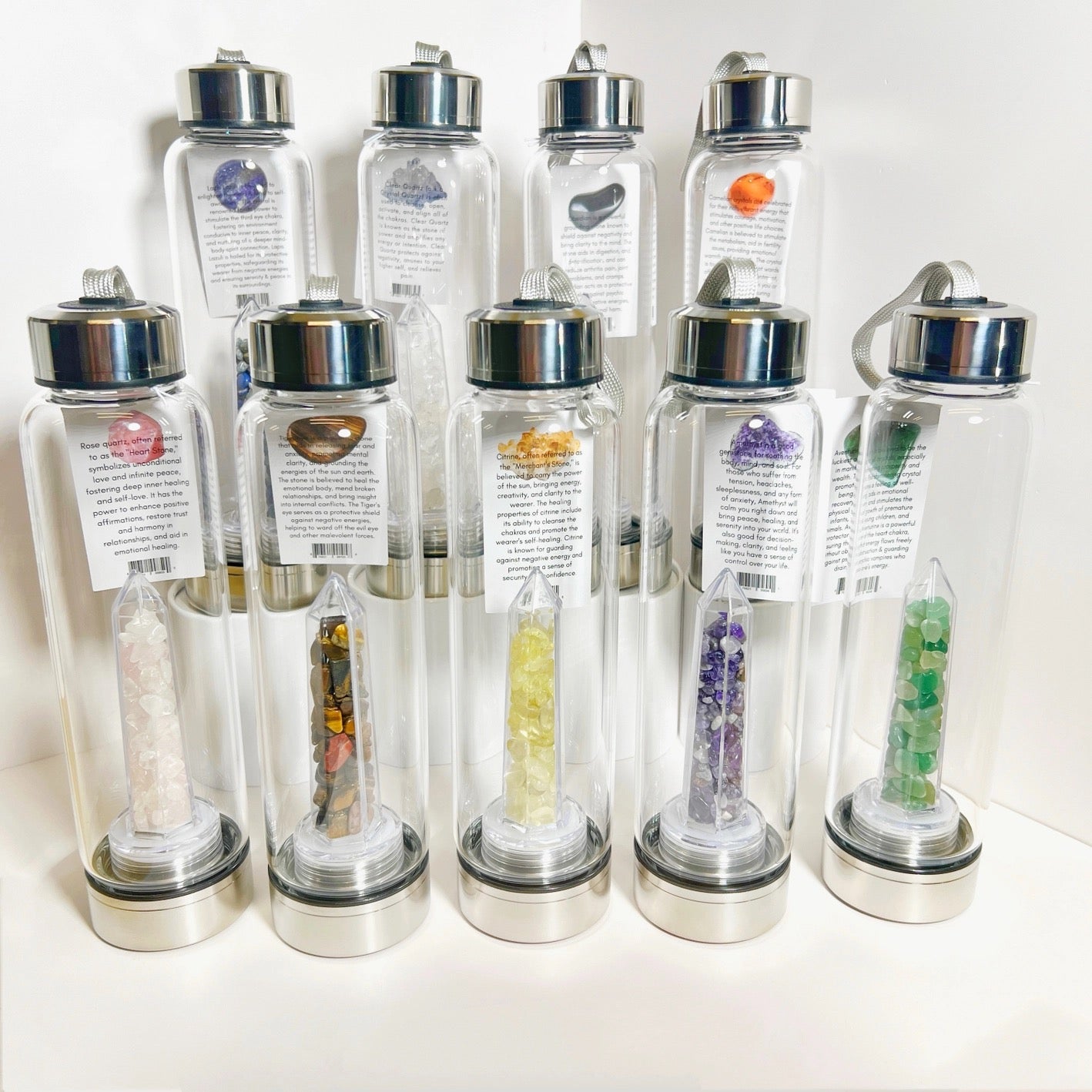 Set of clear water bottles with silver lids, each containing different colored stones or crystals.