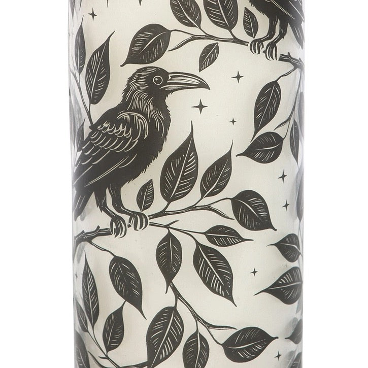 Tall cylindrical candle with black bird and leaf pattern on a white background