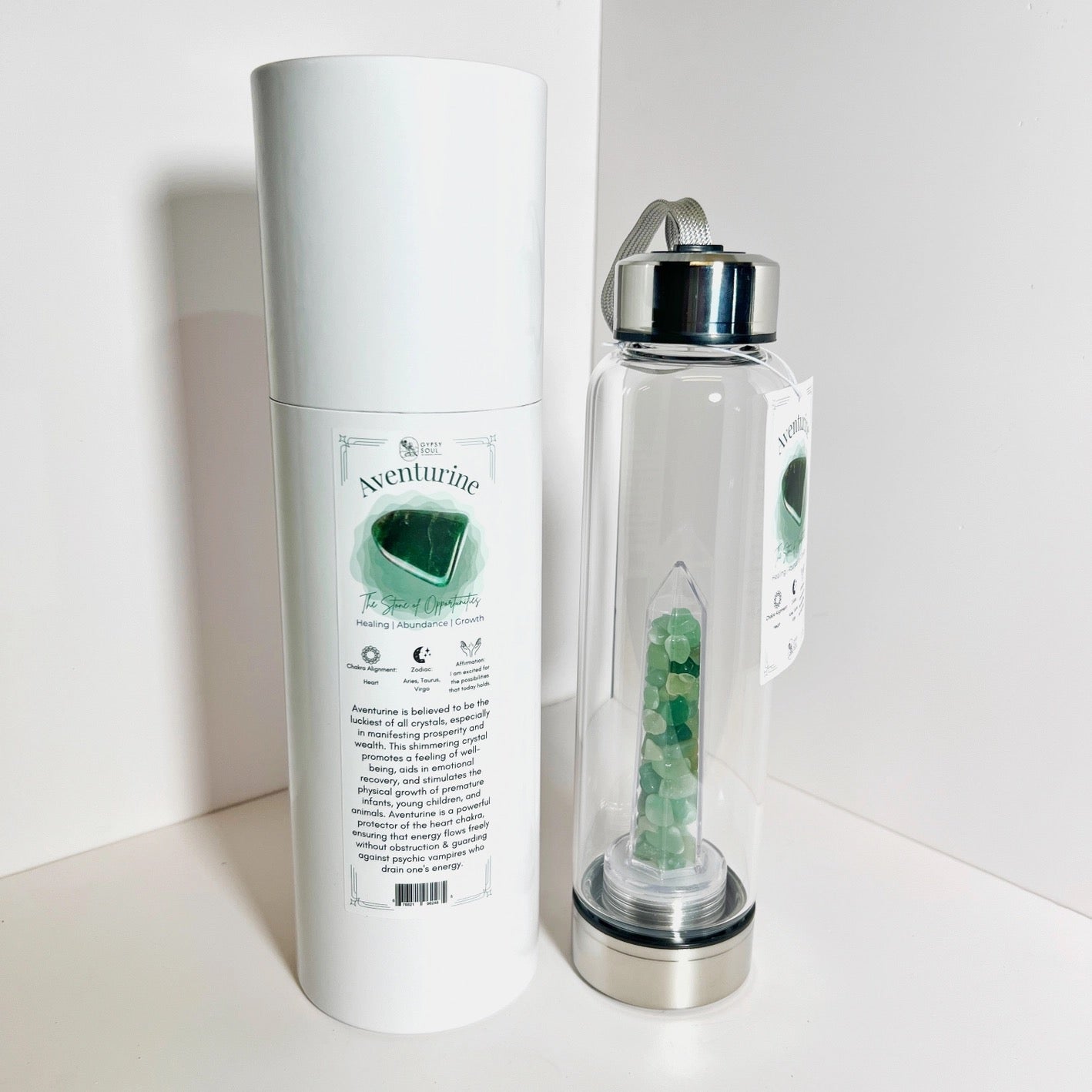 Clear water bottle with green gemstones and white cylindrical container on a white background