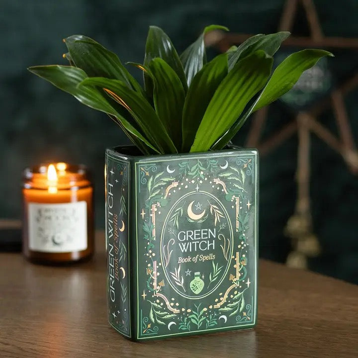 Green Witch book of spells with a lit candle on a wooden surface