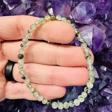 Hand wearing a green beaded bracelet with a purple crystal formation in the background