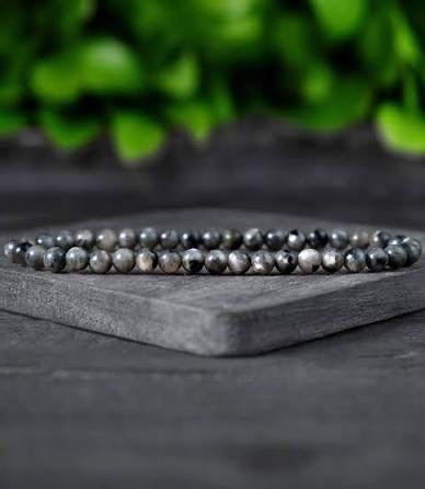 One black and silver beaded bracelet on a dark surface with a blurred green background