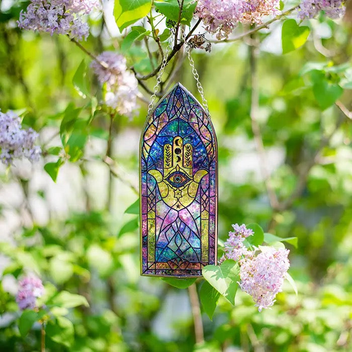 Stained glass window hanging with Hamsa design among lilac flowers