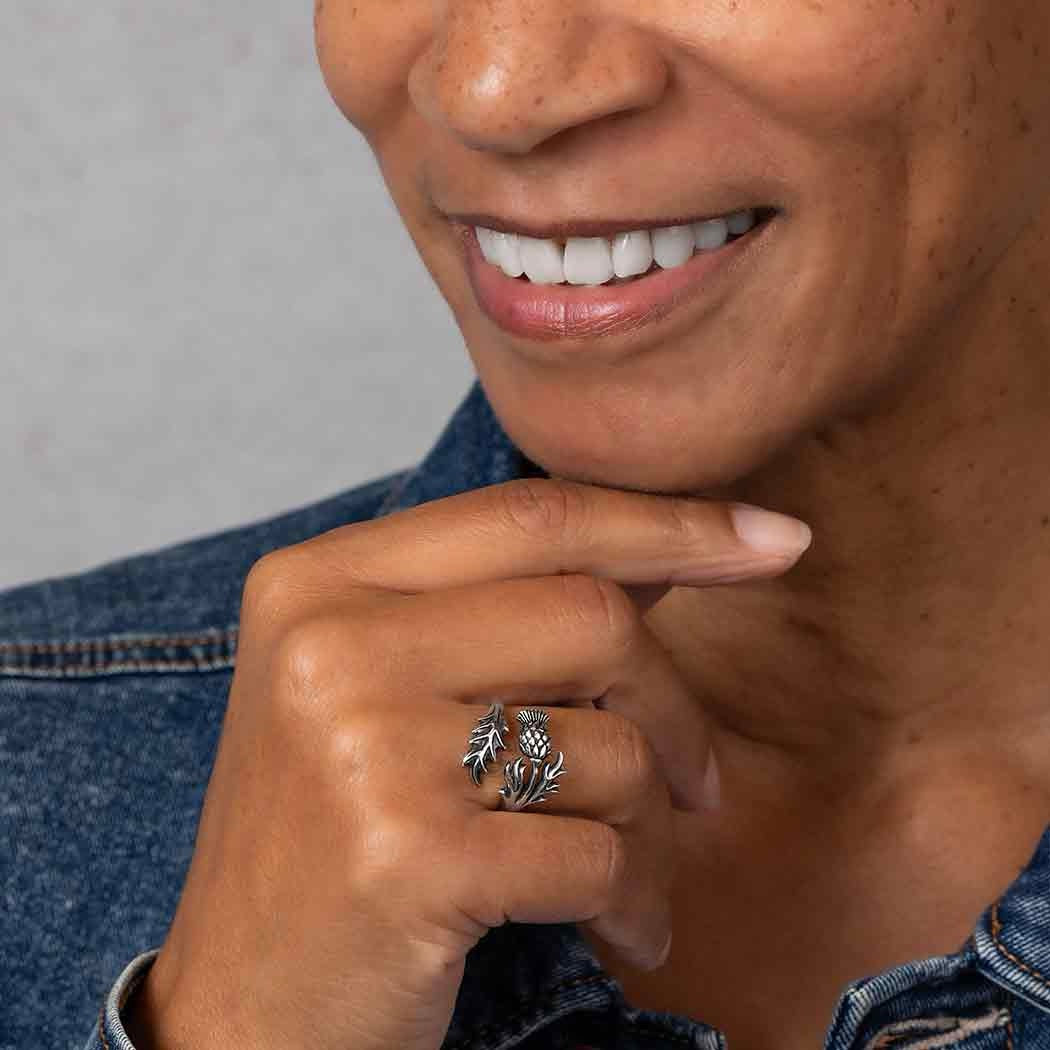 Person wearing a silver ring with a Thistle design on a gray background
