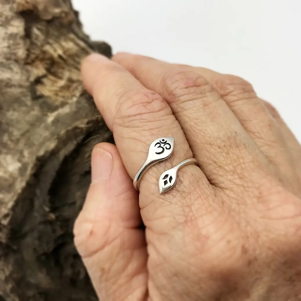 Silver rings with Lotus and Om symbol design on a hand against a wooden background