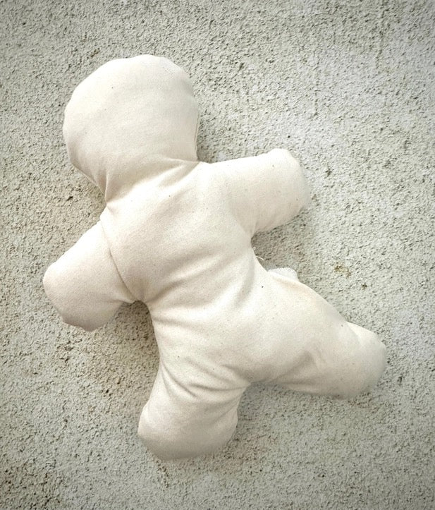 Unfinished white doll stuffed figure on a textured gray surface
