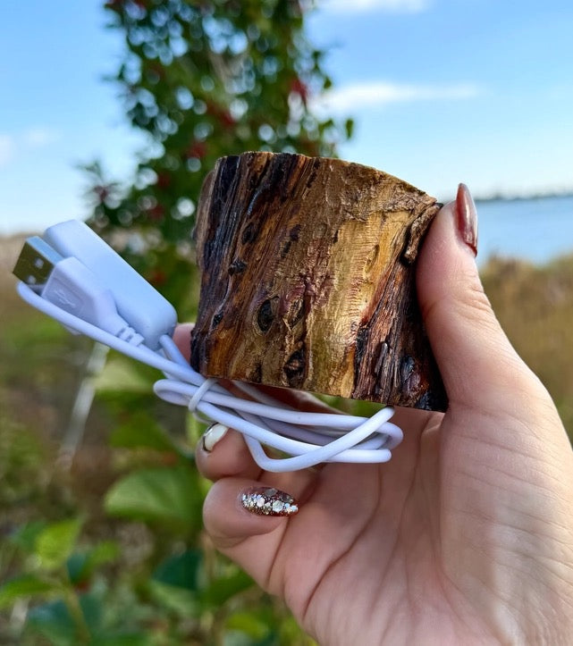 Hand holding a white USB cable with a wooden block outdoors