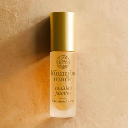 A bottle of Kuumba Made Tunisian Jasmine Fragrance Oil with a metallic gold cap and frosted glass bottle, set against a textured beige background.