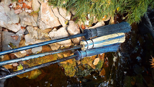 Two brooms leaning against a stone wall with greenery