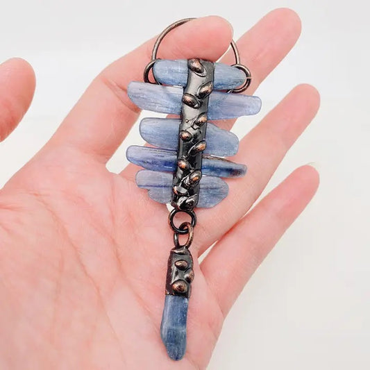 Pendant with blue stones and metal accents held in a hand against a white background