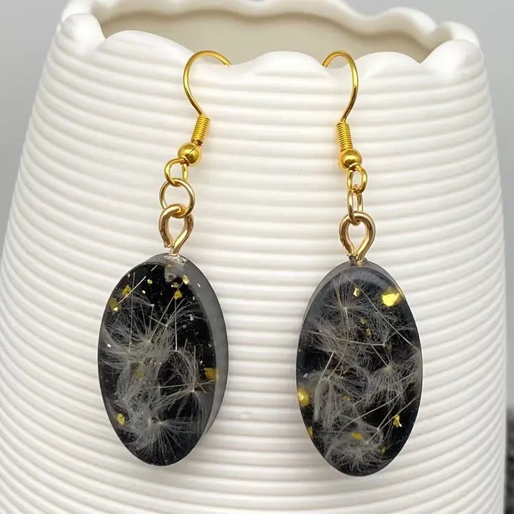 Black oval earrings with gold hooks on a white textured surface