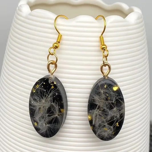 Black oval earrings with gold hooks on a white textured surface