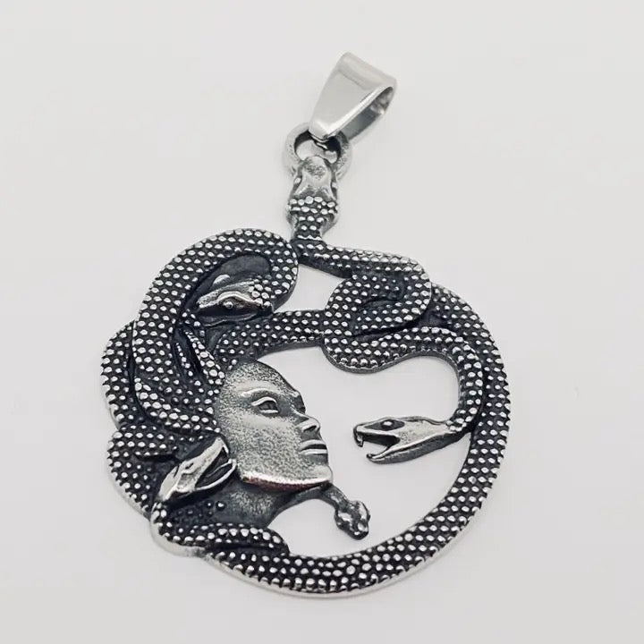 Silver pendant with a snake and human face design on a white background