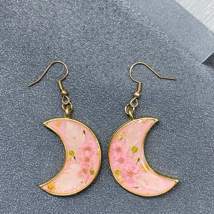 Pink crescent moon earrings with floral design on a gray surface