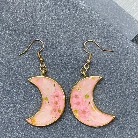 Pink crescent moon earrings with floral design on a gray surface