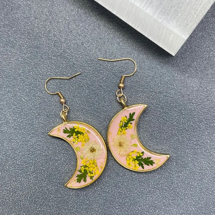 Crescent moon-shaped earrings with floral design on a gray surface