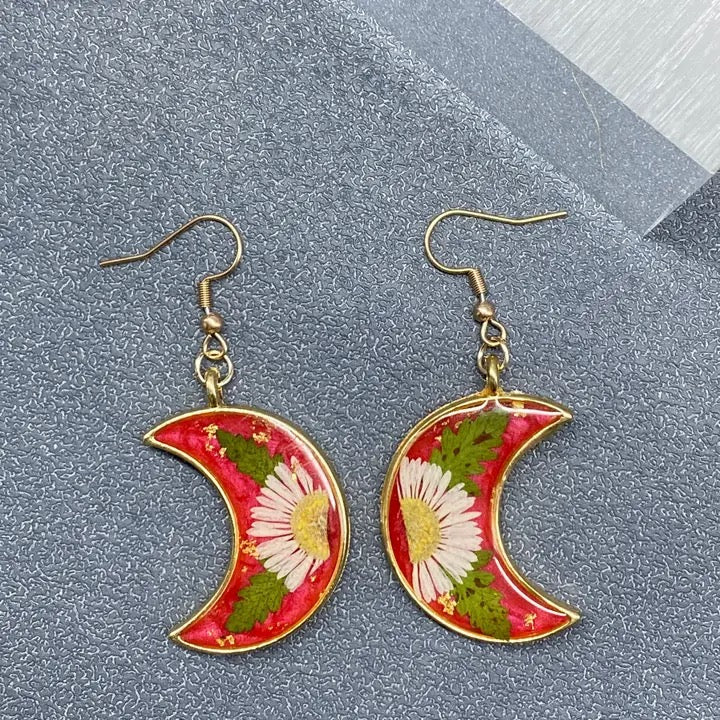 Crescent moon-shaped earrings with floral design on a gray surface